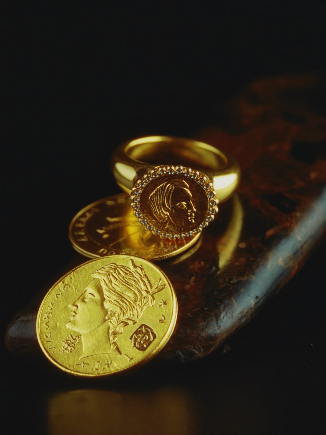 Goldmünzen und ein feiner Ring auf dunklem Stein